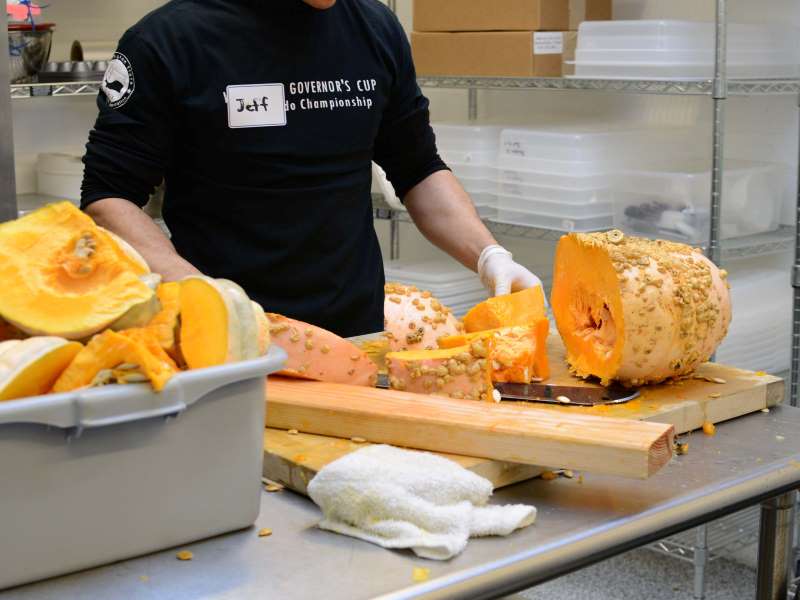 Volunteer preparing a bright orange squash in our downtown repack kitchen to include with the fresh items in our Thanksgiving food distributions.